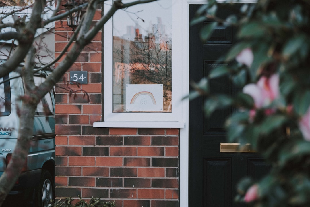 Real estate 'For Sale' sign stands in the manicured front yard of a quiet, empty suburban home, illustrating a property si...