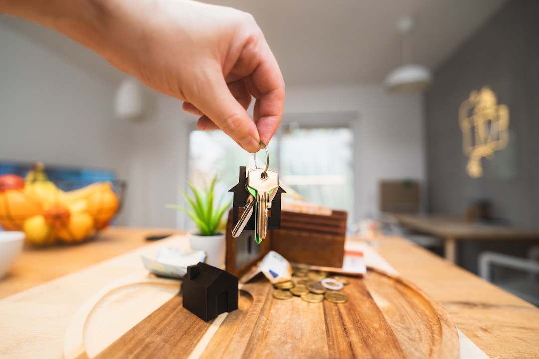 A close-up, brightly lit photo of a person's hand inserting a coin into a house-shaped piggy bank, illustrating the financial savings from a 1% real estate commission.