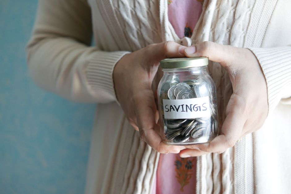 A close-up of a person's hand placing a coin into a clear glass jar, symbolizing the act of saving money on real estate commissions.