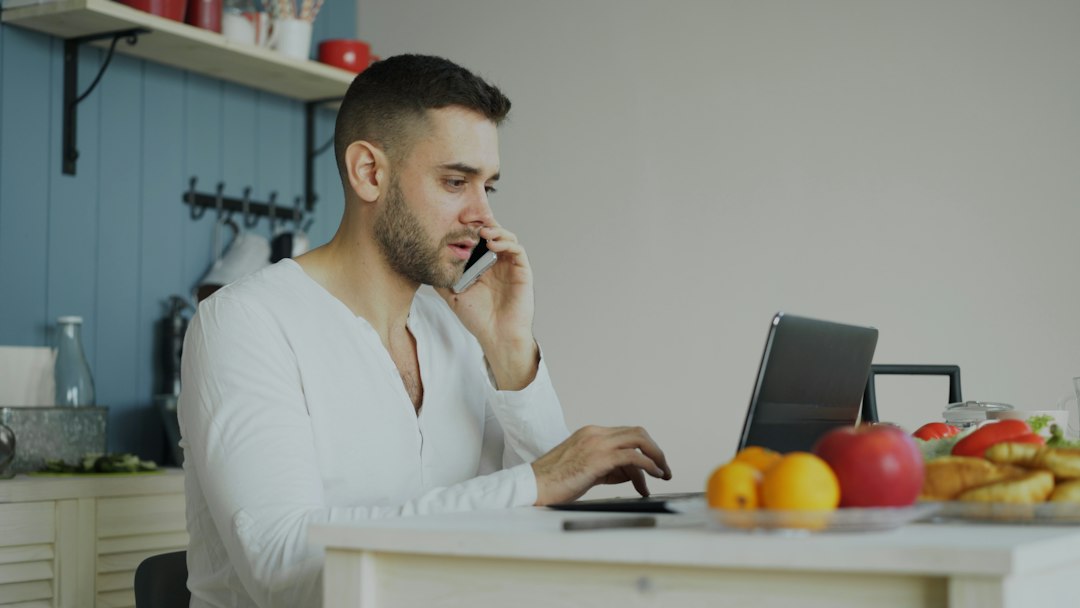 A person sits at a modern kitchen table with a concerned expression, reviewing a stack of real estate papers and a calculator, representing the financial stress of selling a home.